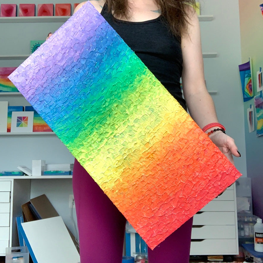 Camille Gerrick holding a textured rainbow gradient painting in her studio