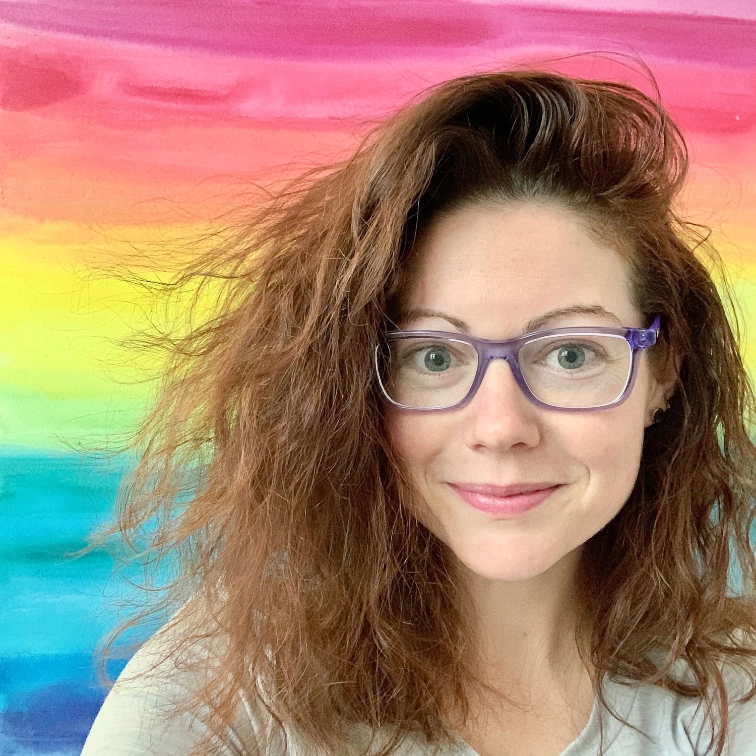 photo of Camille Gerrick smiling wearing purple glasses with a painted rainbow backdrop