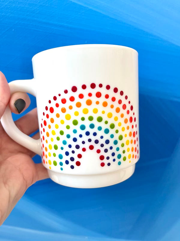 Person holding Vintage-style Rainbow Dot textured Teacup in front of blue background. Made by Camille Gerrick.