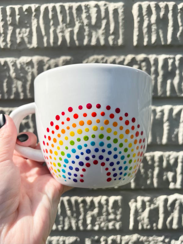 Hand holding a Porcelain Colorful Short Latte Mug with hand-painted dotted ROYGBIV rainbow by Camille Gerrick in direct sunlight in front of concrete wall