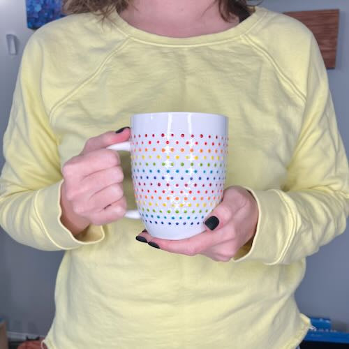 Person holding Porcelain Vibrant Rainbow Dot Tall Latte Mug with bands of textured rainbow dots wrapping around it. Made by Camille Gerrick.