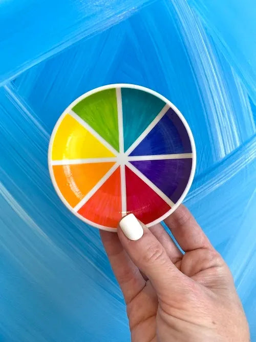 Color wheel rainbow trinket dish held up against blue painted background by Camille Gerrick